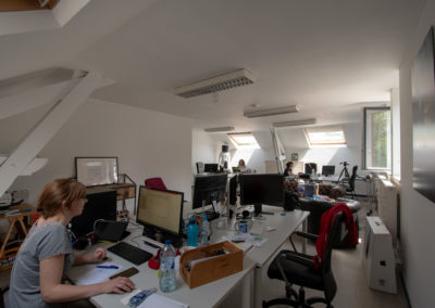 Pièce mensardée agencée en open space (personnes travaillant sur ordinateur sur des groupements de bureaux).